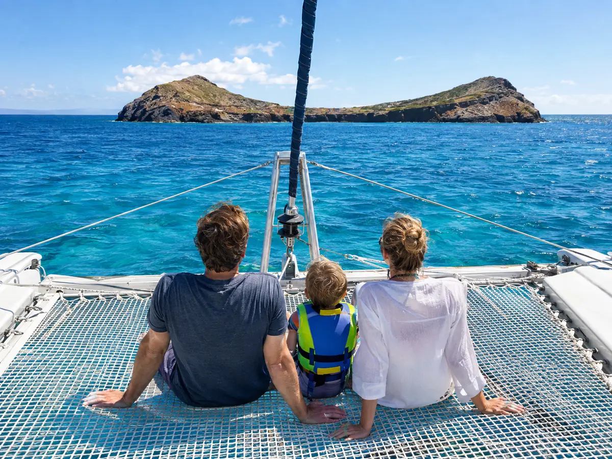 A family sitting on the bow net of a catamaran, a child in a life vest, looking at Molokini
